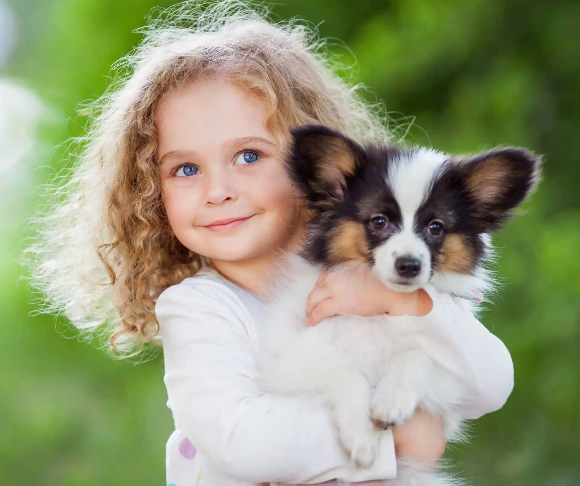 Young girl with curly hair holding a corgi puppy